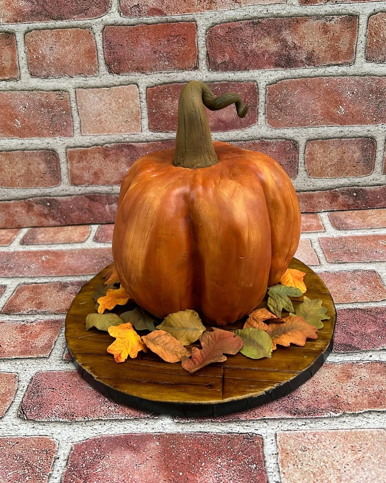 Sculpted pumpkin cake in autumn orange with a fondant stem and fallen leaves