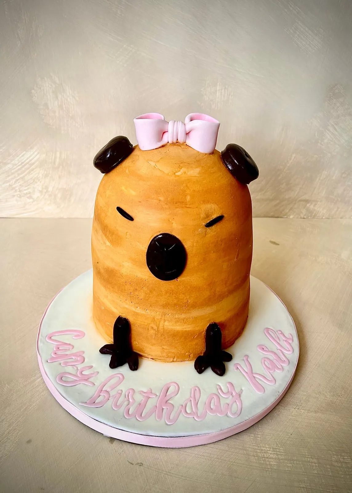 Sculpted bear cub cake in golden fondant with pink bows