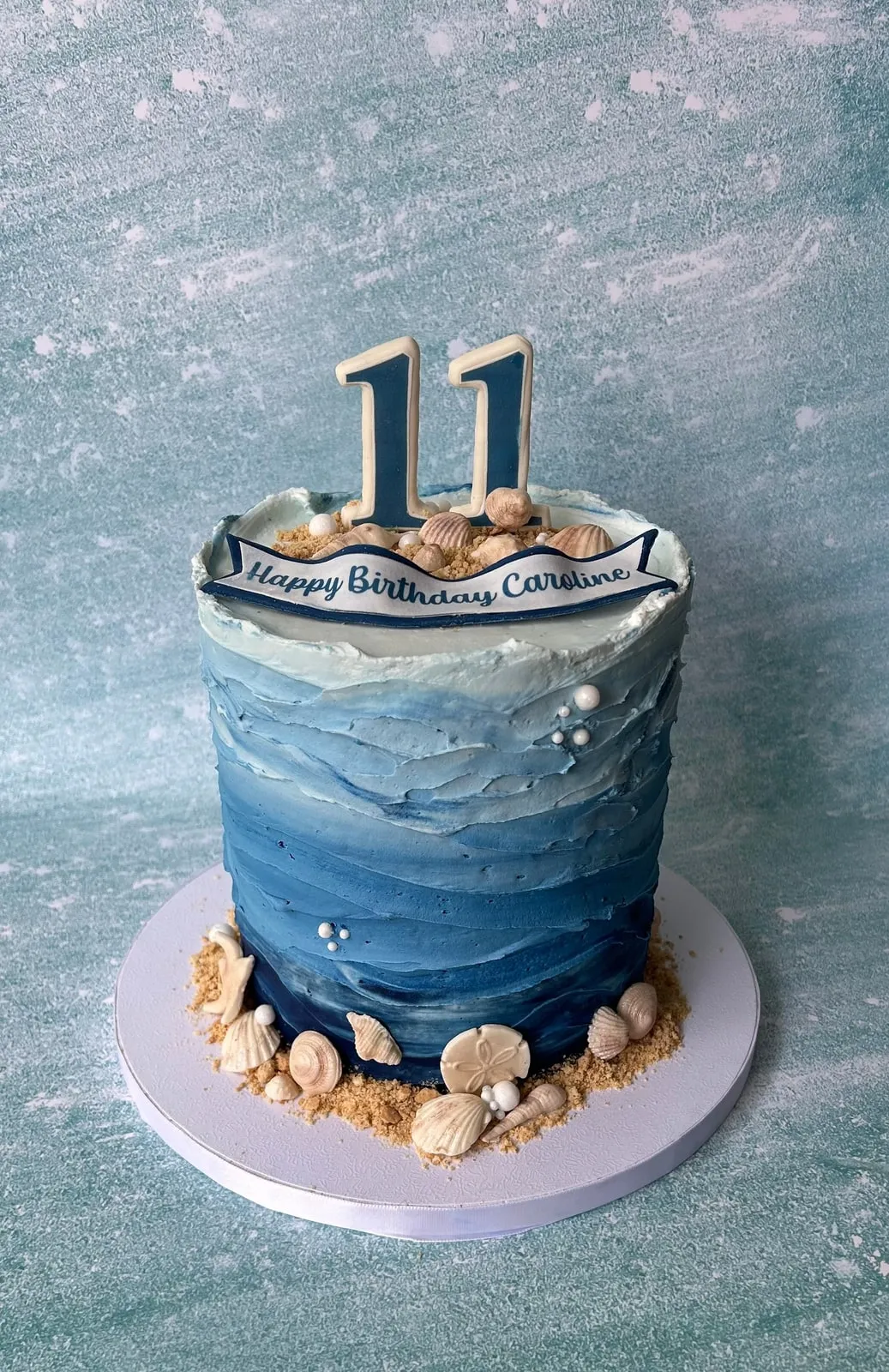 Blue watercolour buttercream birthday cake with gold accents and a shell base