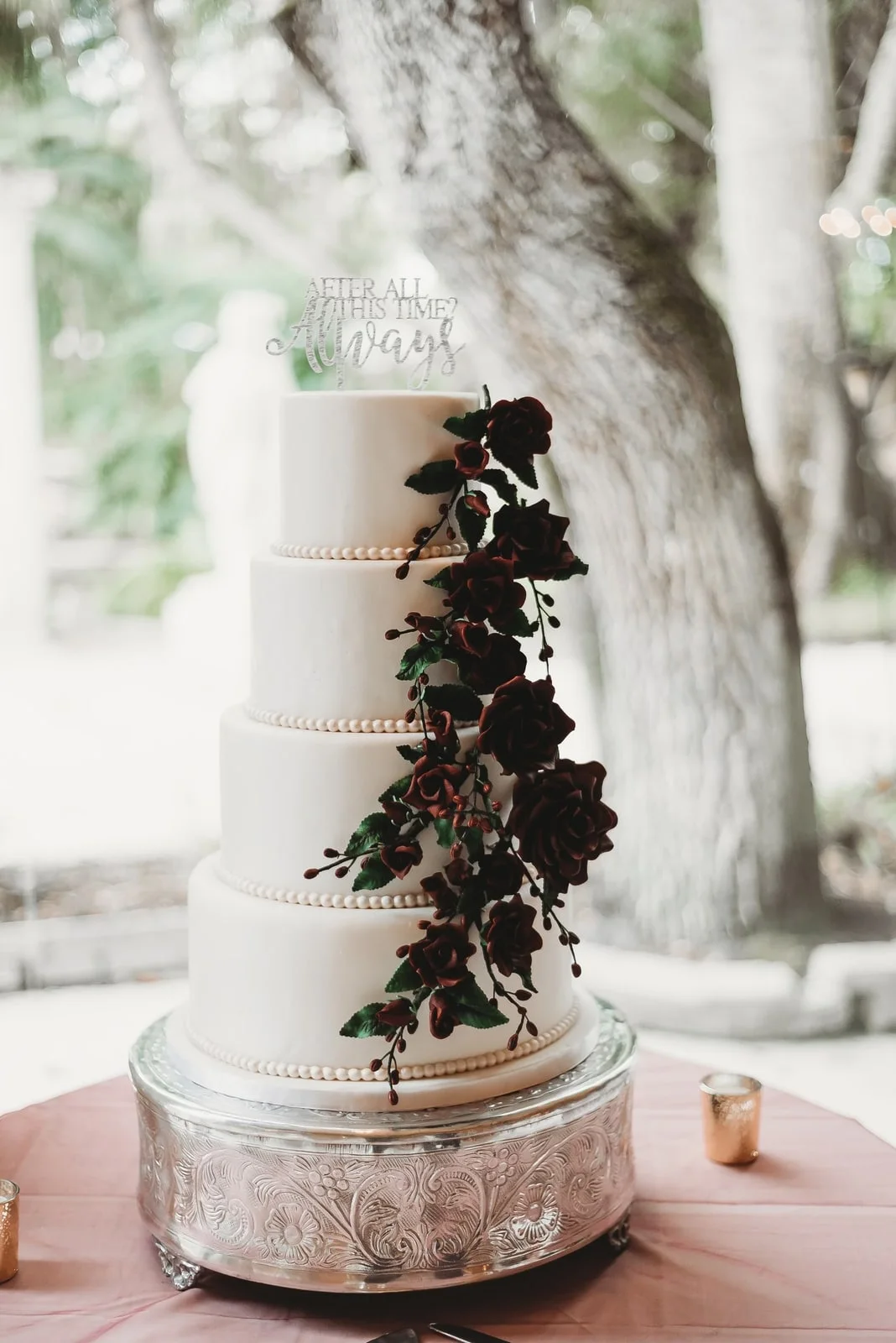 Four tier white wedding cake with cascading burgundy sugar roses and pearl borders