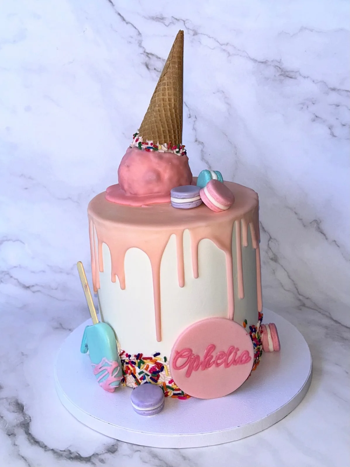 Pink drip birthday cake with a toppled ice cream cone, macarons and sprinkles
