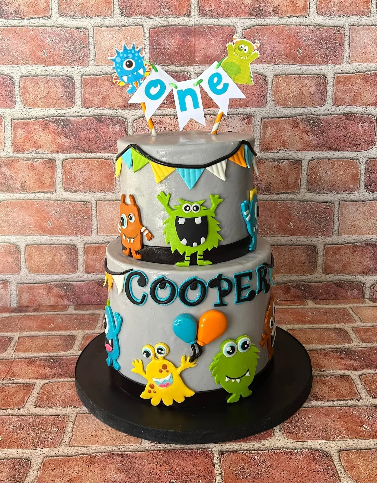 Grey two tier first birthday cake with colourful fondant monsters and a ONE banner