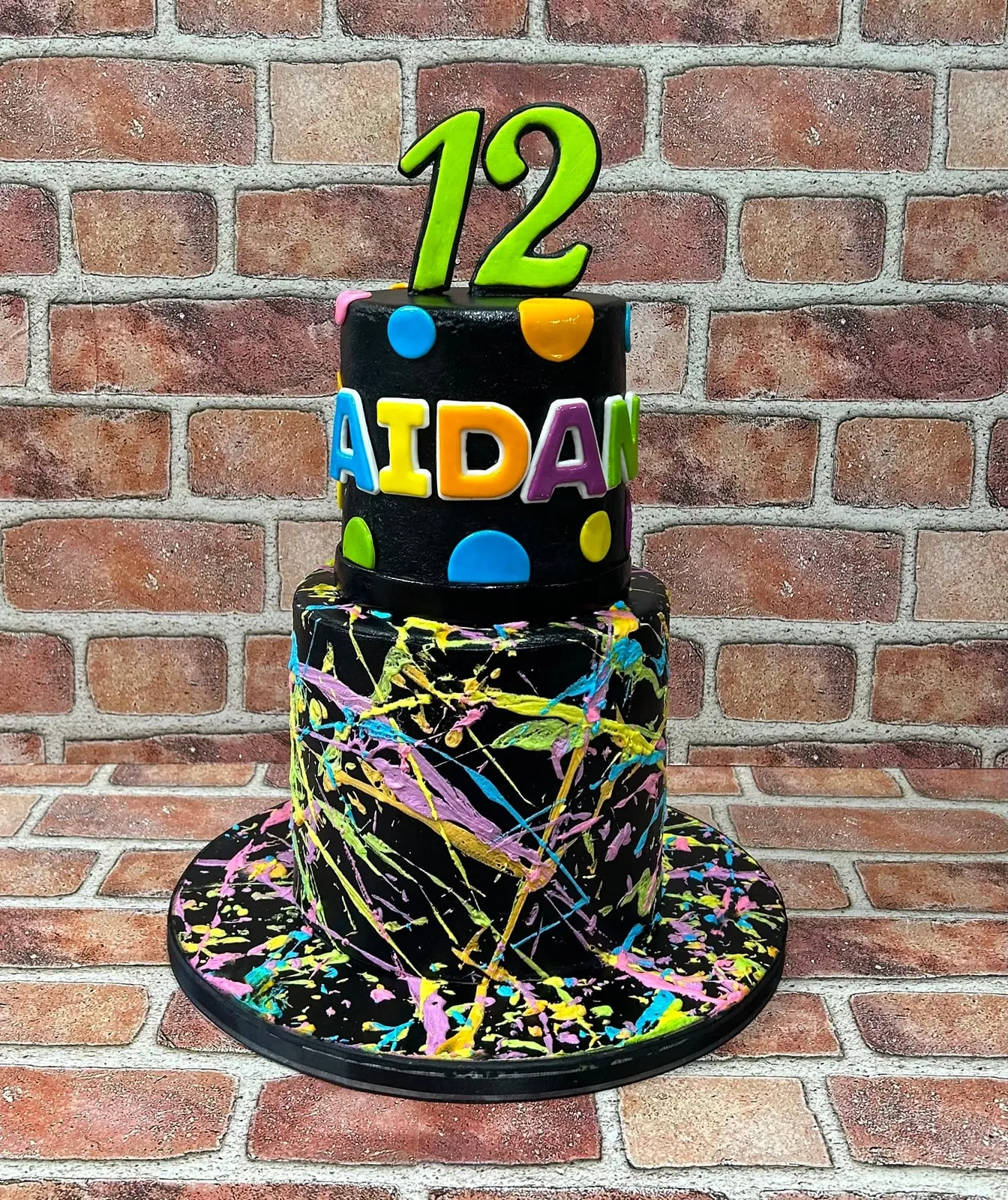 Black two tier birthday cake with neon paint splatter and bright fondant letters