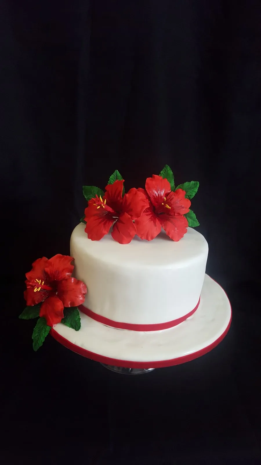 Two tier white wedding cake with a red ribbon and sugar hibiscus flowers