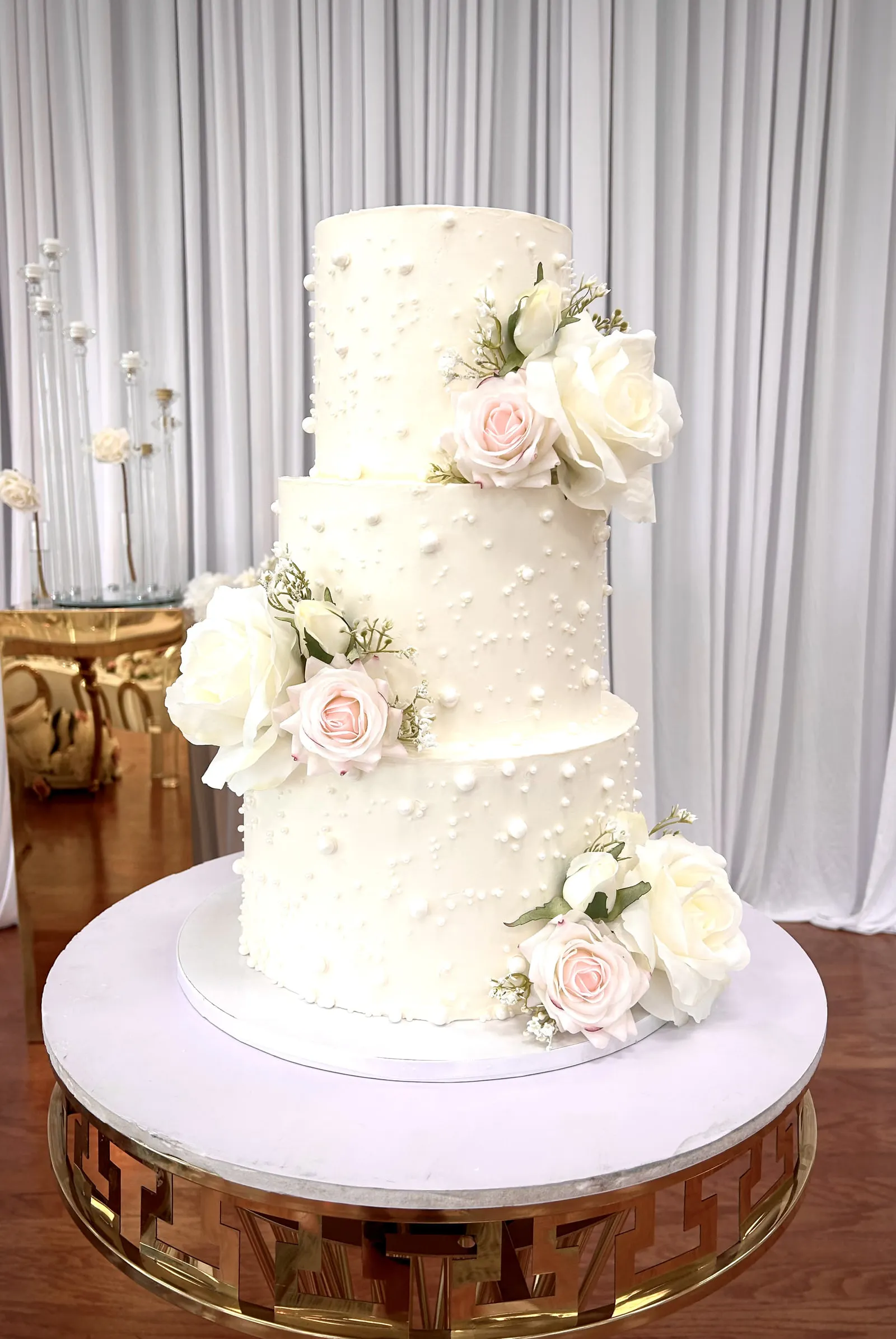 Three tier ivory buttercream wedding cake dotted with piped pearls and clusters of blush and cream roses
