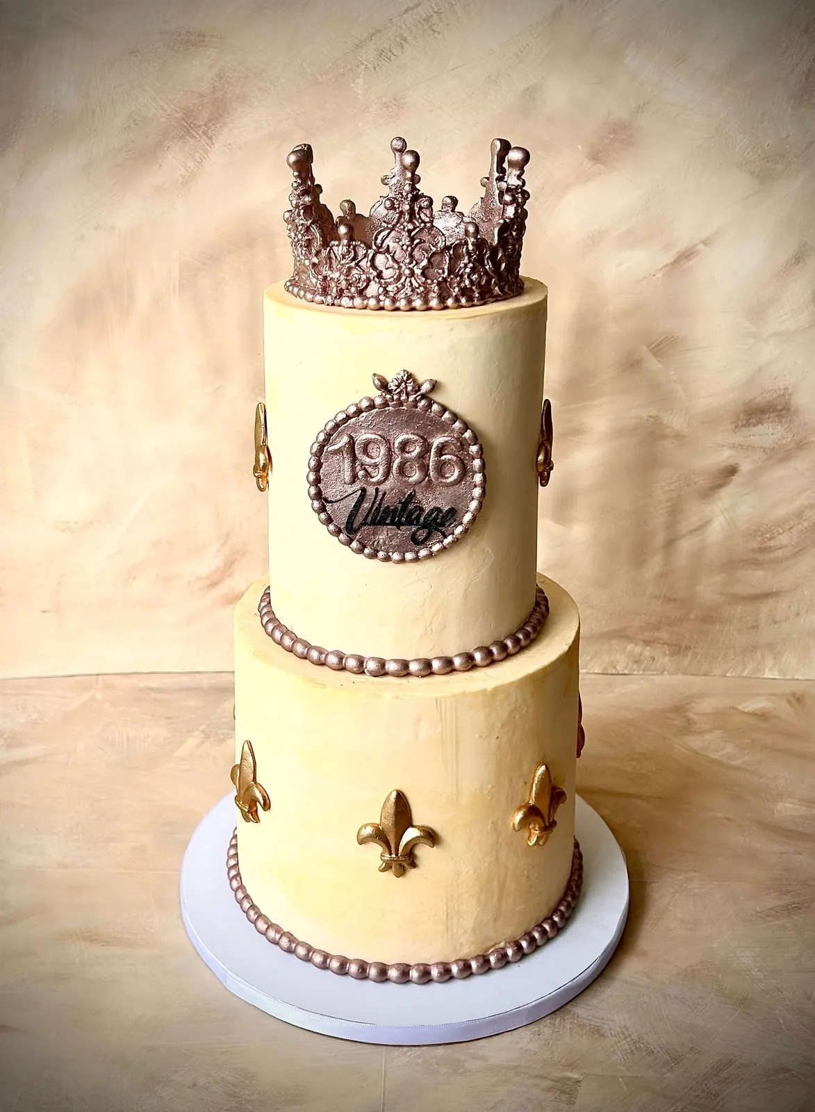 Two tier cream and rose gold milestone birthday cake with a sugar crown, fleur-de-lis and a 1986 Vintage plaque