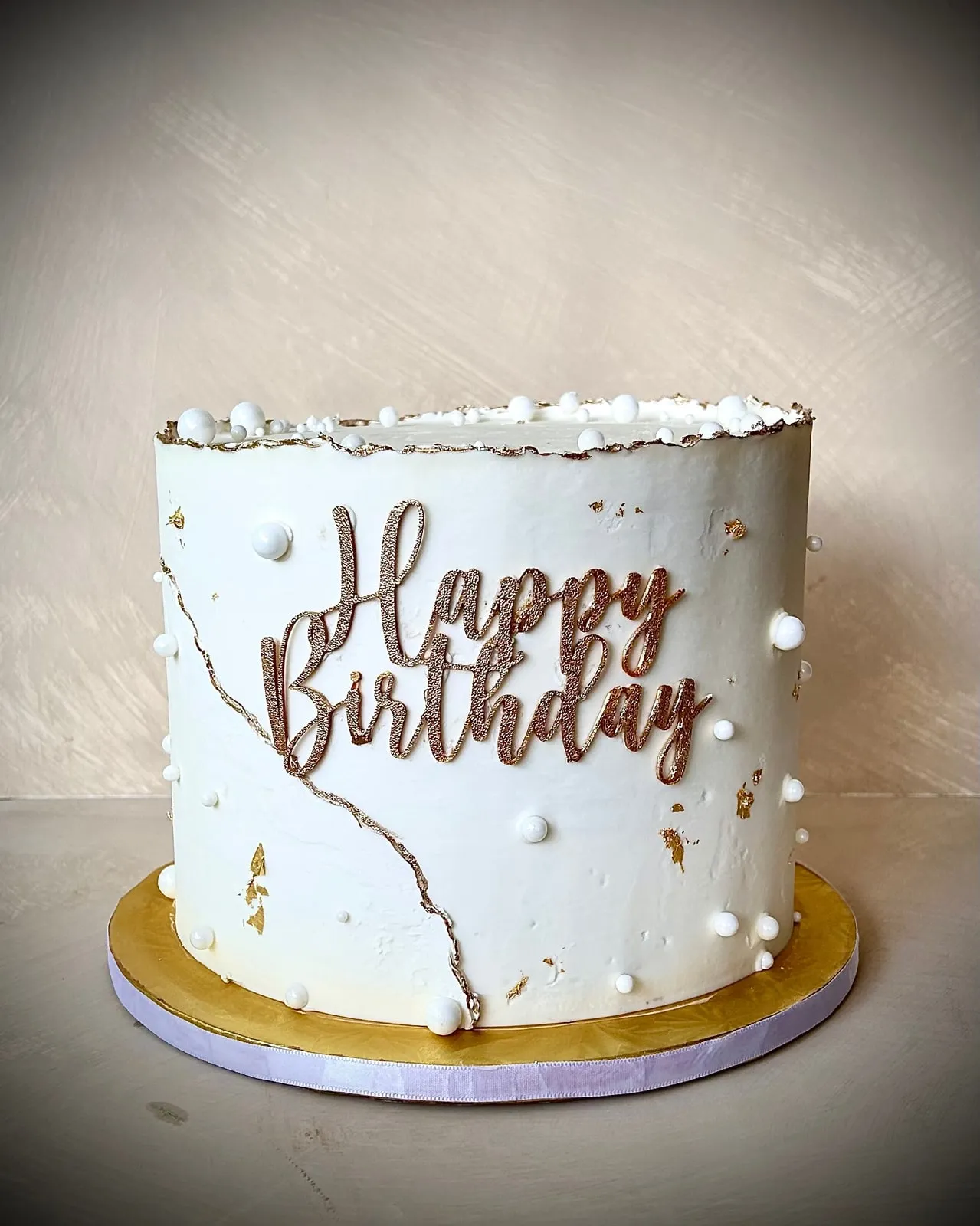 White buttercream birthday cake with gold drip, gold lettering and sugar pearls
